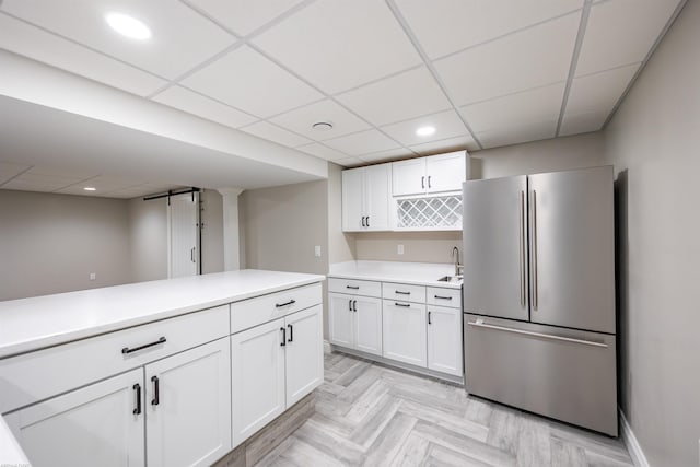 kitchen featuring sink, a paneled ceiling, stainless steel refrigerator, white cabinets, and light parquet floors