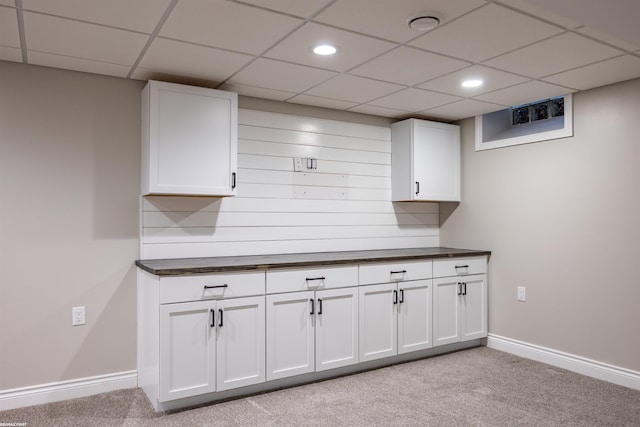 kitchen with light colored carpet, a drop ceiling, and white cabinets