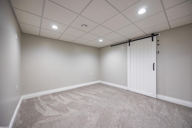 spare room with a barn door, carpet, and a drop ceiling