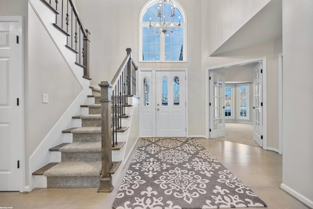 foyer entrance with an inviting chandelier, a towering ceiling, and light wood-type flooring