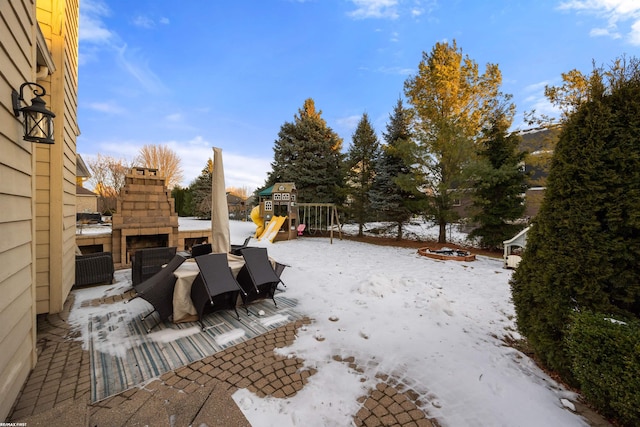 yard covered in snow with a playground and an outdoor stone fireplace