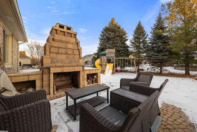 snow covered patio featuring a playground and an outdoor stone fireplace