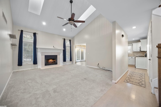 unfurnished living room with a tiled fireplace, a wealth of natural light, light colored carpet, and ceiling fan