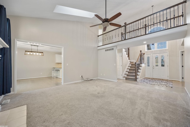 unfurnished living room featuring a towering ceiling, a skylight, light colored carpet, and ceiling fan