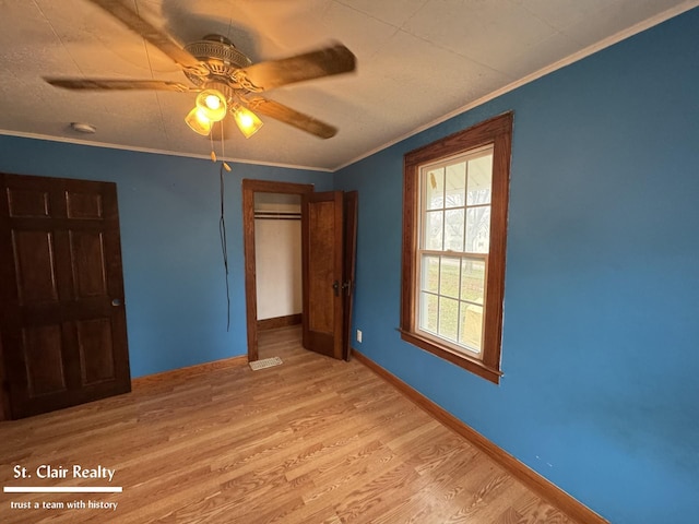 unfurnished bedroom with ceiling fan, ornamental molding, light wood-type flooring, and a closet