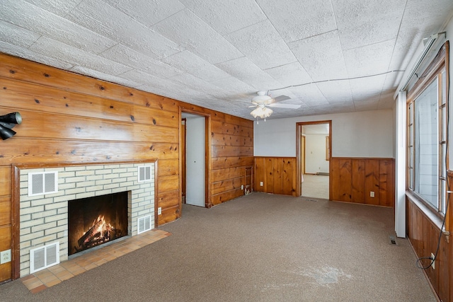 unfurnished living room featuring a fireplace, light colored carpet, ceiling fan, and wood walls