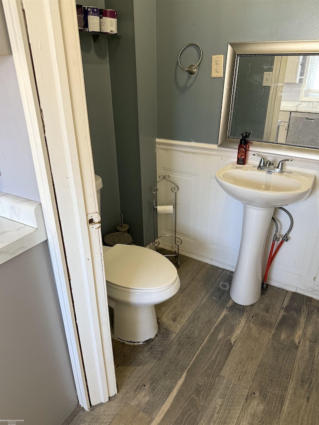 half bathroom featuring a wainscoted wall, toilet, a decorative wall, and wood finished floors