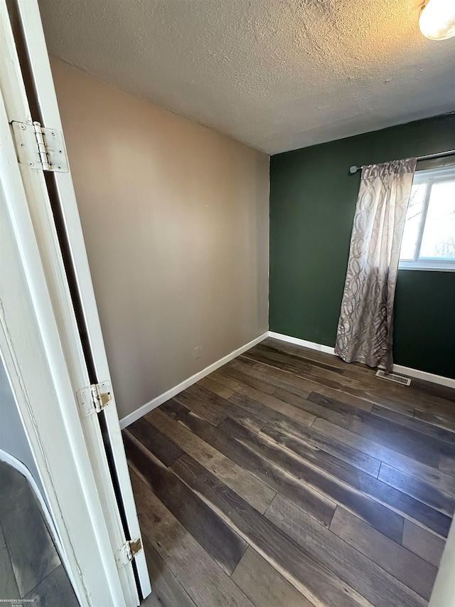 empty room featuring visible vents, baseboards, dark wood-type flooring, and a textured ceiling