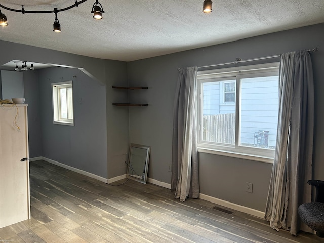 empty room with baseboards, arched walkways, visible vents, and wood finished floors