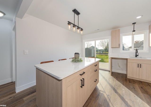 kitchen with pendant lighting, sink, light stone counters, a kitchen island, and light brown cabinets