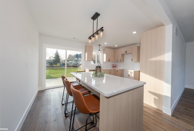 kitchen featuring pendant lighting, a kitchen island, wood-type flooring, a kitchen bar, and light brown cabinetry