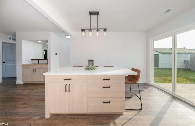 kitchen featuring light brown cabinetry, hardwood / wood-style flooring, pendant lighting, and a center island