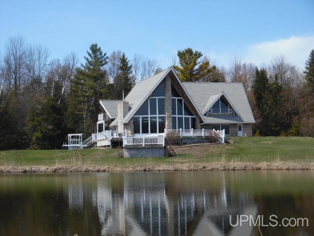 rear view of house with a deck with water view and a yard