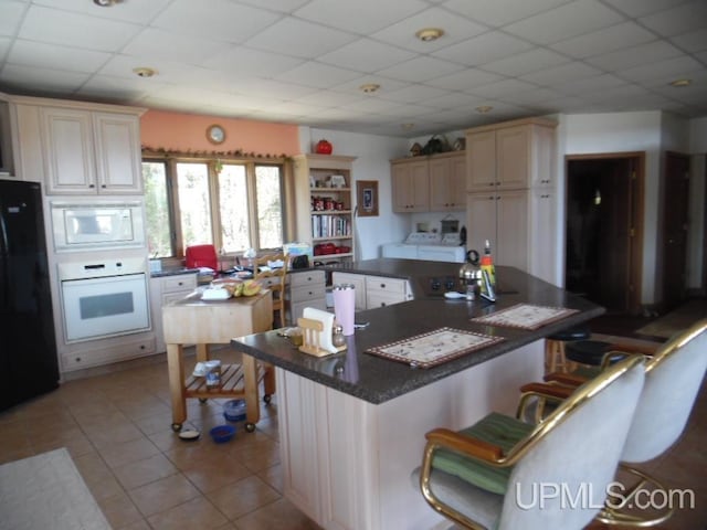 kitchen with a kitchen island, a drop ceiling, white appliances, and cream cabinetry