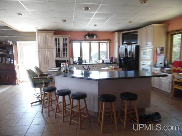 kitchen with a kitchen island, a paneled ceiling, a kitchen breakfast bar, white appliances, and cream cabinetry