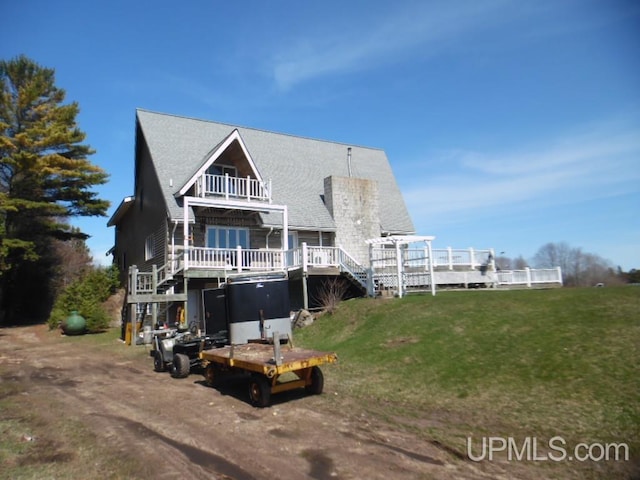 back of property with a balcony, a deck, and a lawn