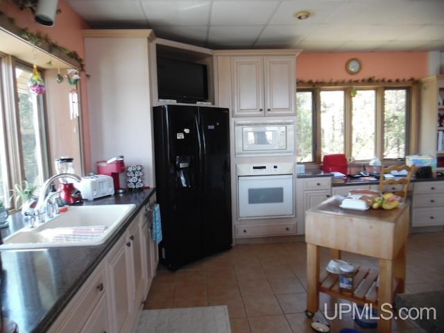 kitchen featuring light tile patterned flooring, white appliances, plenty of natural light, and a paneled ceiling