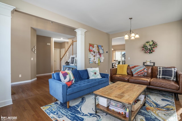 living room featuring dark wood-type flooring, a notable chandelier, and ornate columns