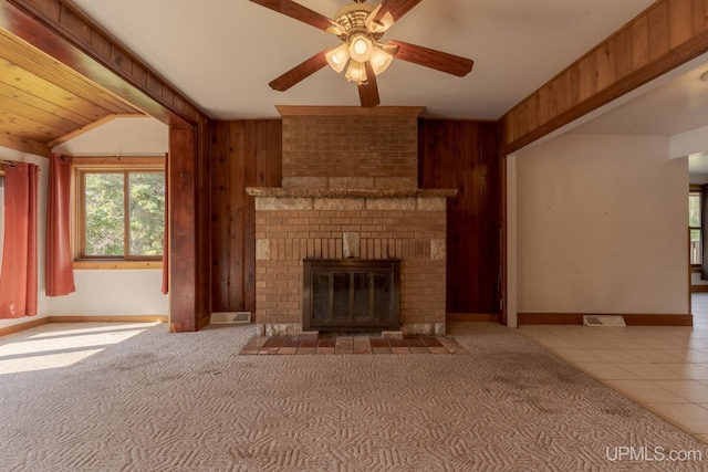 unfurnished living room with ceiling fan, wooden walls, carpet floors, a fireplace, and vaulted ceiling