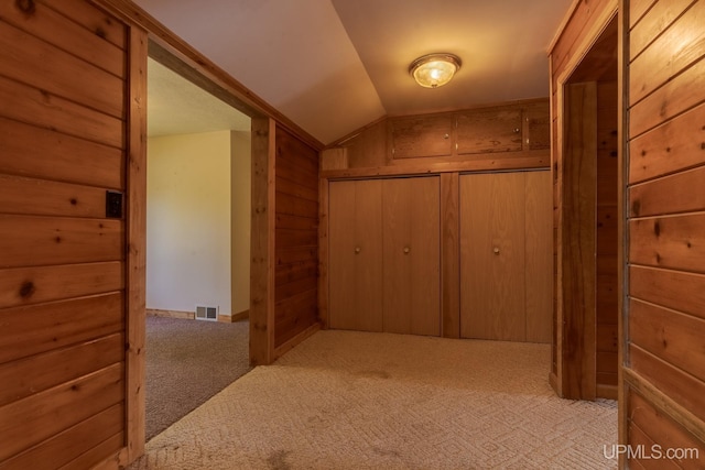 hallway with light colored carpet, vaulted ceiling, and wood walls