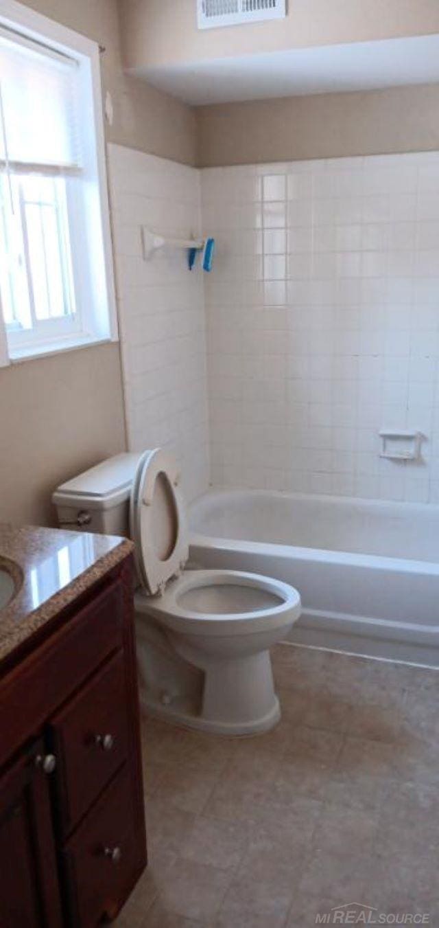 full bathroom featuring vanity, tiled shower / bath combo, and toilet