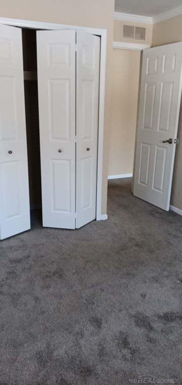 unfurnished bedroom with ornamental molding, a closet, and dark colored carpet