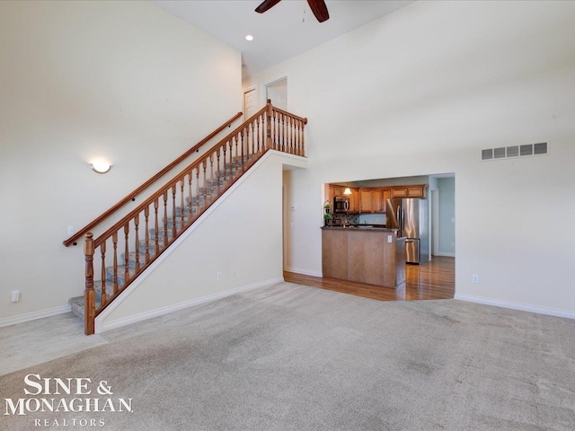 unfurnished living room with ceiling fan, light carpet, and a high ceiling