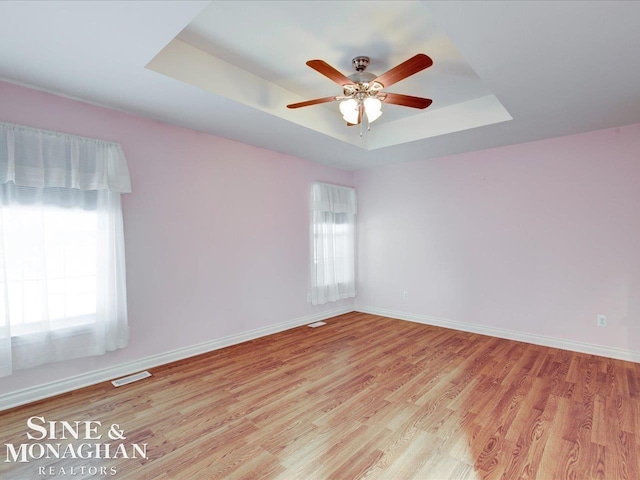 unfurnished room with a tray ceiling, a wealth of natural light, light hardwood / wood-style floors, and ceiling fan