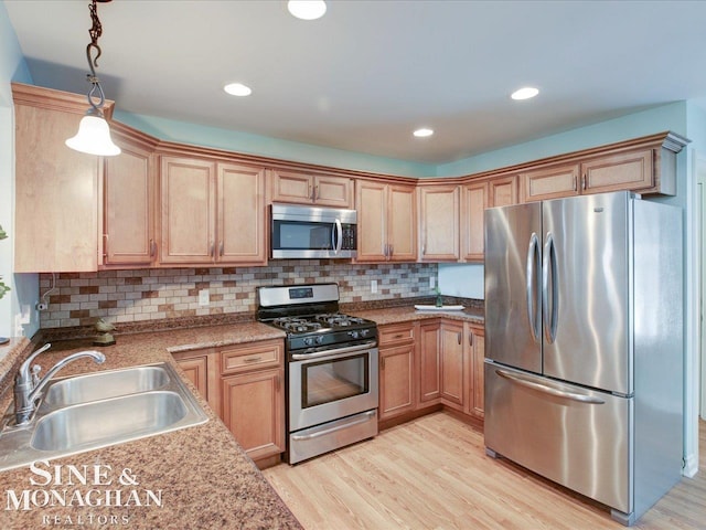 kitchen with sink, pendant lighting, stainless steel appliances, light hardwood / wood-style floors, and backsplash