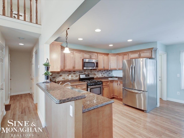 kitchen featuring appliances with stainless steel finishes, pendant lighting, dark stone counters, light hardwood / wood-style floors, and kitchen peninsula