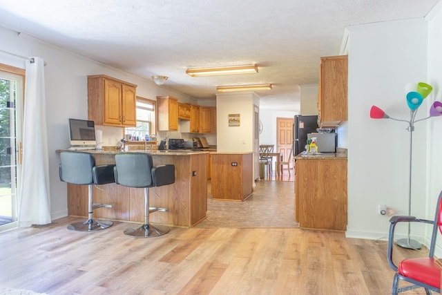 kitchen featuring a breakfast bar area, refrigerator, kitchen peninsula, dark stone counters, and light wood-type flooring