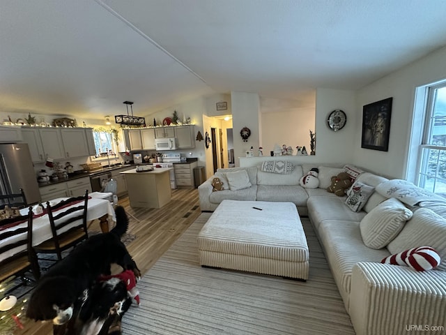 living room featuring vaulted ceiling, sink, and light hardwood / wood-style floors