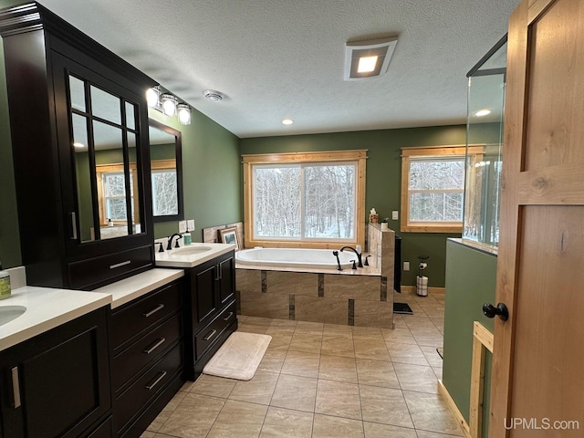 bathroom with vanity, a relaxing tiled tub, tile patterned floors, and a textured ceiling