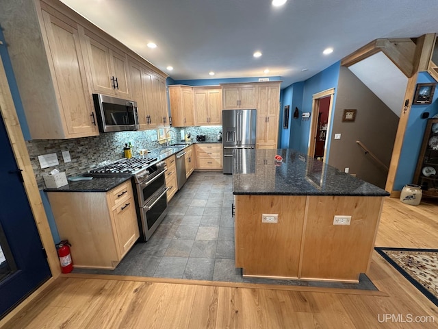 kitchen featuring decorative backsplash, dark stone counters, a center island, stainless steel appliances, and light hardwood / wood-style flooring