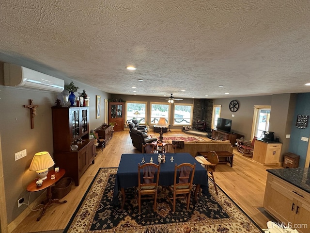 dining room featuring a wall mounted air conditioner, light hardwood / wood-style floors, and a textured ceiling