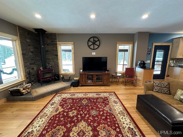 living room featuring a wood stove, a wealth of natural light, a textured ceiling, and light hardwood / wood-style floors