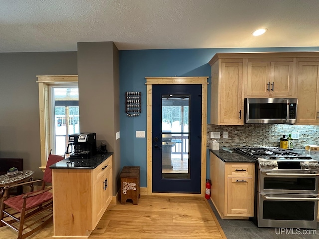 kitchen with stainless steel appliances, dark stone countertops, light brown cabinetry, and light hardwood / wood-style flooring