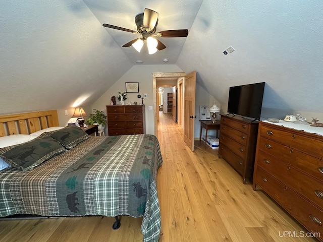 bedroom with a textured ceiling, vaulted ceiling, light hardwood / wood-style floors, and ceiling fan