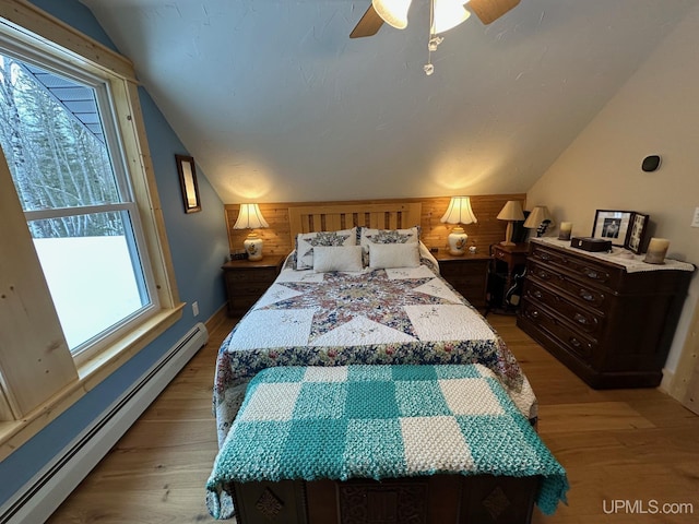 bedroom featuring lofted ceiling, ceiling fan, baseboard heating, light hardwood / wood-style floors, and wood walls