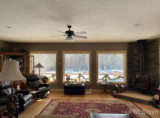 living room with ceiling fan, light hardwood / wood-style flooring, a textured ceiling, and a wood stove