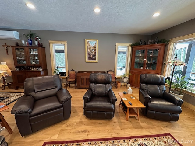 living room with a wall mounted air conditioner, light hardwood / wood-style floors, and a textured ceiling