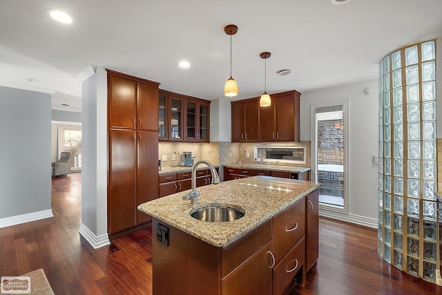 kitchen with sink, light stone counters, hanging light fixtures, a center island with sink, and decorative backsplash