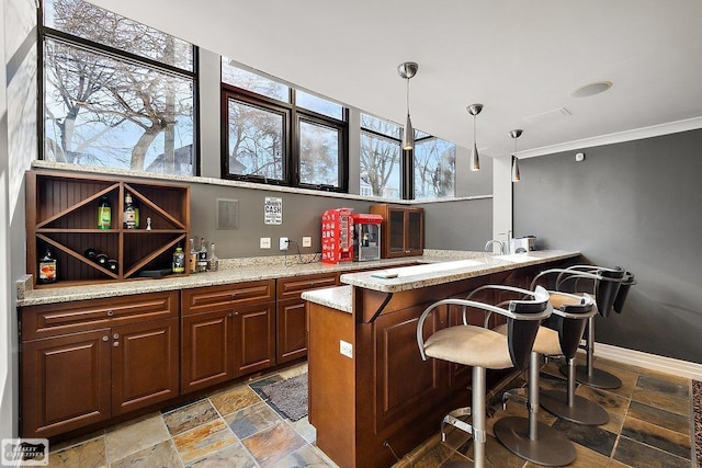 bar featuring ornamental molding, light stone countertops, and hanging light fixtures