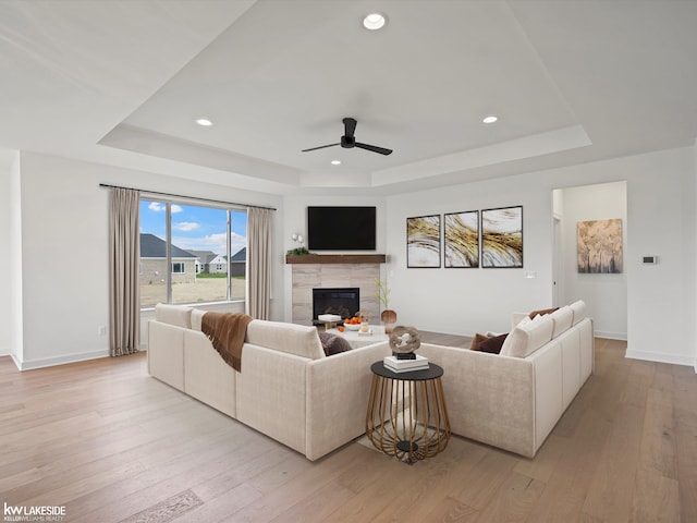 living room with ceiling fan, a fireplace, light wood-type flooring, and a tray ceiling