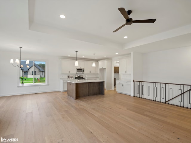 kitchen with appliances with stainless steel finishes, pendant lighting, white cabinetry, a center island with sink, and light wood-type flooring