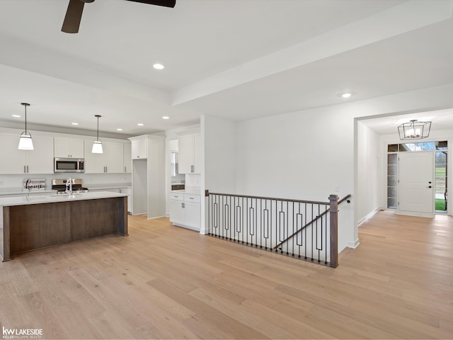 kitchen with stainless steel appliances, light wood-type flooring, hanging light fixtures, and white cabinets