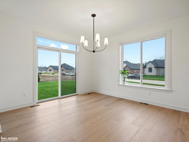 unfurnished room with a healthy amount of sunlight, a chandelier, and light wood-type flooring