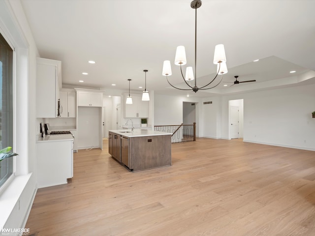 kitchen with sink, hanging light fixtures, an island with sink, light hardwood / wood-style floors, and white cabinets