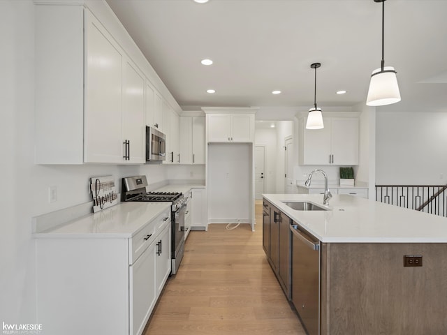 kitchen with sink, appliances with stainless steel finishes, a kitchen island with sink, white cabinets, and decorative light fixtures