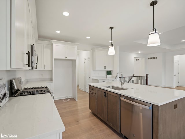 kitchen with stainless steel appliances, an island with sink, pendant lighting, and white cabinets